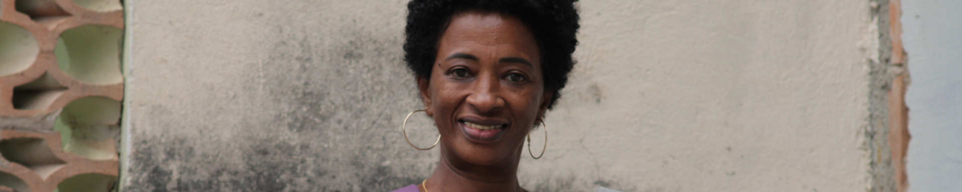Uma mulher negra com mochila nas costas, segurando uma pasta e sorrindo para a foto